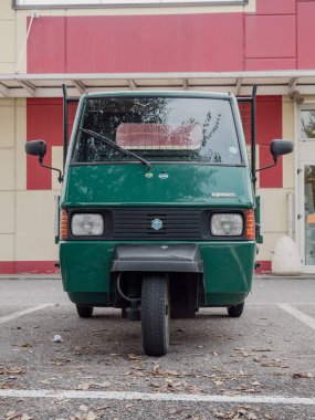 Arquato, PC, İtalya - 31 Ekim 2024 Kırmızı ve bej bir binanın önünde park etmiş yeşil bir maymun piaggio kargo kamyonetinin ön görüntüsü, üç tekerlekli tasarımı sergileniyor.