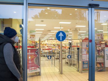 Cremona, Lombardy, İtalya 27 Ekim 2024 Koruyucu yüz maskesi takan müşteri Coronavirus salgını sırasında süpermarkete otomatik kapılardan giriyor.