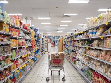 Cremona, Lombardy, İtalya 27 Ekim 2024 raflarla dolu raflar arasında süpermarket koridorunda duran boş alışveriş arabası, alışveriş veya tüketim kavramının başladığını öne sürüyor.