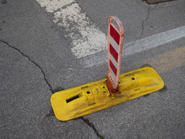 Cremona, Lombardy, Italy October 27th 2024 Red and white striped delineator post on yellow base indicating a no parking zone on an asphalt road, ensuring traffic safety and flow clipart