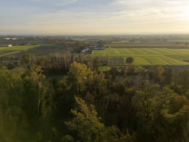 Ağaçları ve uzakta küçük bir köyü olan güzel yeşil bir tarla. Gökyüzü mavi ve beyaz bulutların karışımıdır.
