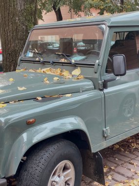 Piacenza, İtalya 15 Ekim 2024 Green Land Rover defans oyuncusu bir şehir sokağına park etmiş, düşen sonbahar yapraklarıyla süslenmiş, sert ama şık bir cazibe yayıyor.