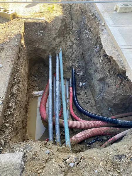 Piacenza, İtalya 15 Ekim 2024 Renkli elektrik kabloları ve kanalları, altyapı veya kamu hizmetleri çalışmaları sırasında yerin altına kazılan bir siperde görülebilir.