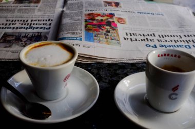 Cremona, Lombardy, İtalya - 7 Kasım 2024 Cappuccino ve espresso bir İtalyan gazetesinin yanında koyu benekli bir yüzey üzerinde oturuyorlar.