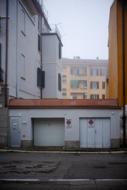 Cremona, Lombardy, İtalya - 7 Kasım 2024 İtalya 'da sisli bir günde iki beyaz garaj kapısı ve gri bir yaya kapısı
