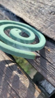 Yeşil sivrisinek kovucu bobin ahşap masada yanıyor, dumanı yayıyor ve dışarıdaki böceklerden korunuyor.