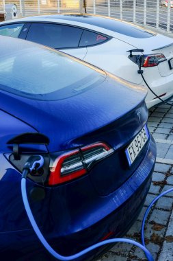 Cremona, Ially - 6 Ekim 2024 İki Tesla modeli 3 elektrikli araç, sürdürülebilir ulaşım ve çevre dostu teknoloji sergileyerek, bir kamu şarj istasyonunda pillerini şarj ediyorlar.