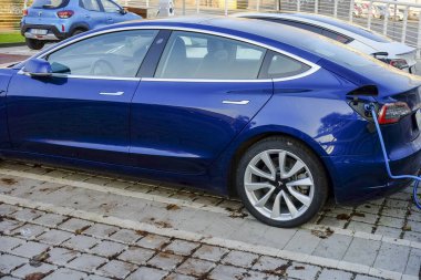 Cremona - 6 Ekim 2024 Deep Blue metalik tesla modeli 3 uzun menzilli çift motorlu tüm tekerden çekişli şarj istasyonu bataryasını şarj ediyor