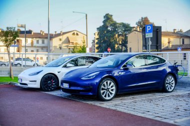 Cremona, Ially - 6 Ekim 2024 İki Tesla modeli 3 elektrikli araba, biri mavi, biri beyaz, şarj edildiği yere park edilmiş.