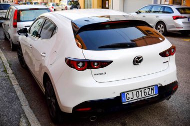 Cremona, genel olarak - 6 Ekim 2024 Beyaz Mazda 3 hatchback 2.0 Skyactiv-x şehir caddesinde park edilmiş, modern tasarımını ve parlak özelliklerini arka plandan vurguluyor