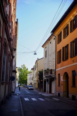 Cremona, İtalya - 7 Kasım 2024 Dar bir caddede güneşli bir günde, tipik bir İtalyan kasabasında renkli binalarla birlikte beyaz minibüs sürüyor