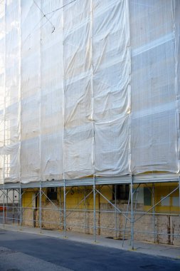 Cremona, İtalya - 7 Kasım 2024 İnşaat sırasında güvenlik ve toz kontrolünün sağlanması için yapı iskelesi ve koruyucu beyaz branda ile kaplanmış yenileme çalışmaları devam ediyor