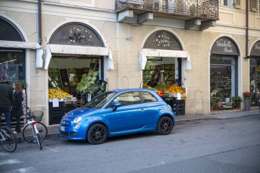 Cremona, İtalya - 15 Kasım 2024 Bir meyve ve sebze dükkanı ve bir çiçekçinin yanındaki Avrupa caddesinde park edilmiş mavi fiat 500 salonu