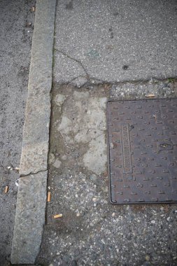 Cremona, İtalya - 20 Kasım 2024 Kaldırım kenarındaki rögar kapağına yakın çekim, etrafa saçılmış sigara izmaritleri ve çatlak kaldırımlarla kentsel çürümeyi vurguluyor