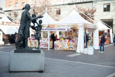 Cremona, İtalya - 20 Kasım 2024 Bronz Antonio Stradivari heykeli, cremona, İtalya 'daki festa del torrone sırasında market tezgahlarında nougat satıyor.
