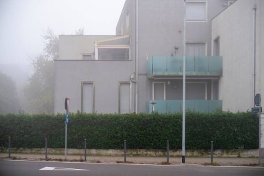 Cremona, İtalya - 20 Kasım 2024 Modern konut binası gri ve bulutlu bir günde yoğun siste kayboluyor, gizemli ve atmosferik bir şehir manzarası yaratıyor.