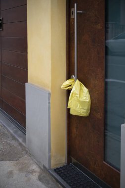 Cremona, İtalya - 20 Kasım 2024 Modern metal kapı kolundan sarkan sarı plastik çanta