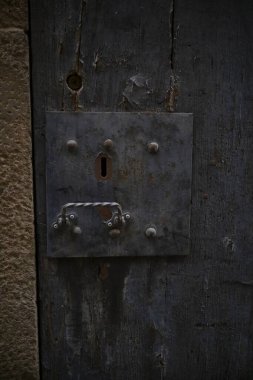 Cremona, Italy - November 20th 2024 Close-up of an old, weathered wooden door featuring a rusty metal lock and handle, evoking a sense of history and security clipart