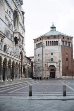 Cremona, İtalya - 20 Kasım 2024 Cremona, İtalya 'da Piazza del Comune' da yürüyen turistler bulutlu bir günde katedrali ve vaftiz törenini ziyaret ediyorlar.