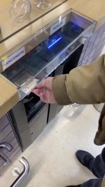 Cremona, İtalya - 9 Aralık 2024 'te yaşlı bir müşterinin elinin bir süpermarketteki kasaya 50 avroluk banknot sokması ve makinenin geri kalanını tükürmesini beklemesi.