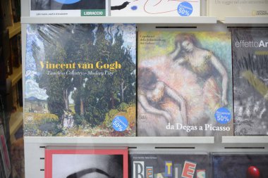 Cremona, İtalya - 24 Aralık 2024 Renkli sanat kitapları, plastiğe sarılı, canlı kapaklar ve başlıklar sergileniyor, kalabalık bir kitapçıda rafta sergileniyor.