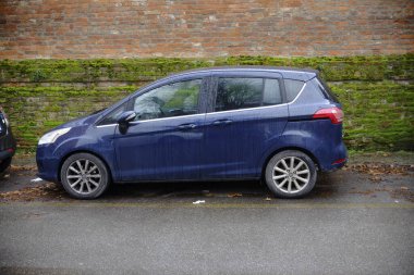 Cremona, İtalya - 24 Aralık 2024 Koyu mavi Ford B-Max sokağın kenarına park etmiş, kısmen yosun kaplı tuğla duvarın yanında.