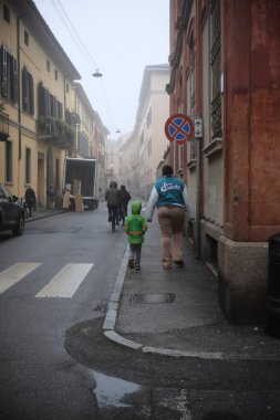 Cremona, İtalya - 15 Ocak 2024 sisli bir sabahta İtalya 'nın Cremona şehrinde serin kış gününün huzurlu atmosferinin tadını çıkarırken anne ve oğlu el ele yürüyorlar.