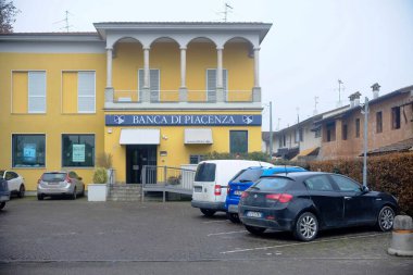 Busseto, Parma, İtalya - 31 Ocak 2025 Kemerler ve balkon gibi klasik mimari detaylara sahip sarı bir banka binası, önünde çok sayıda araba park halinde duruyor. Gün
