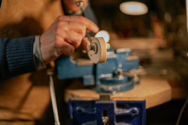 İtalyan Luthier, loş aydınlatılmış bir atölyede özel aletler kullanarak bir kemanın parşömenini dikkatlice hazırlıyor ve geleneksel telli çalgı yapımının titiz sürecini vurguluyor.