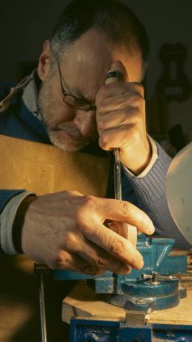 Cremona, İtalya - 6 Şubat 2025 Üstad Luca Tenore loş aydınlatılmış bir atölyede, daha titiz bir şekilde keman parşömenini oyuyor, elleri ustalıkla keskiyi ustalıkla yönlendiriyor..