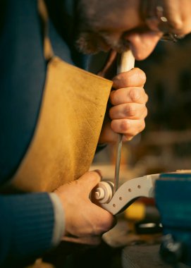 Cremona, İtalya - 6 Şubat 2025 Üstad Luca Tenore önlük giyen İtalyan Luthier, geleneksel bir atölyede uzmanlığını kullanarak yeni bir kemanın kayışını dikkatlice oyuyor..