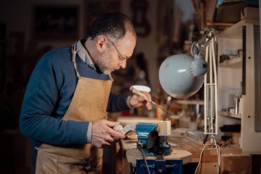 Cremona, İtalya - 6 Şubat 2025 Üstad Luca Tenore İtalyan luthier, önlük ve gözlük takıyor, titizlikle yeni bir keman parşömeni hazırlıyor, ustalıkla bir oyuk ve mengene kullanıyor