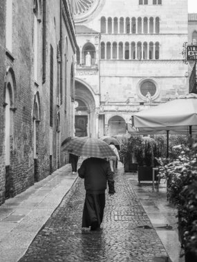 Cremona, İtalya - 9 Şubat 2025 Katolik rahip, İtalya 'nın Cremona kentindeki Santa Maria Assunta Katedrali yakınlarında şemsiyeyle yağmurda yürüyor
