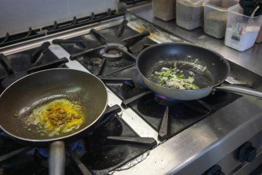 Baharatlar ve tereyağı profesyonel bir gaz sobasında tavada cızırdıyor, başka bir tavada doğranmış soğan ve yeşil biber pişiriliyor, geleneksel bir Hint yemeği hazırlarken.