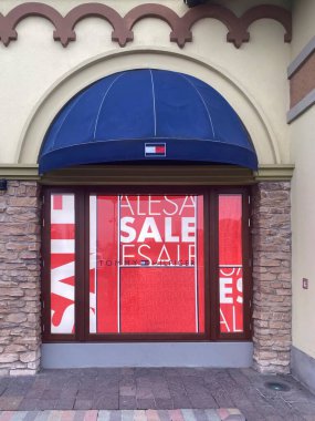 Storefront of Tommy Hilfiger store with sale signs at Fidenza Village, a popular outlet mall in Italy, offering discounts on fashion and designer brands clipart