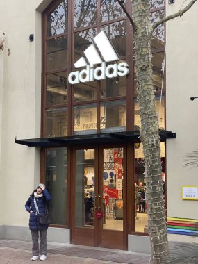 Customer walking and looking at Adidas store at Fidenza Village, a luxury outlet shopping mall in Italy clipart