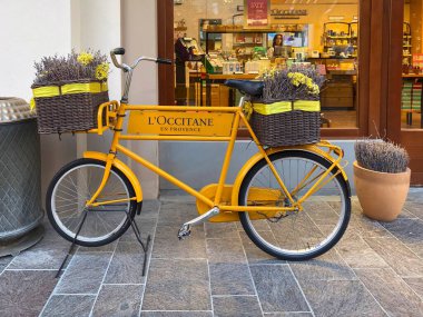 Yellow vintage bicycle with wicker baskets full of lavender promoting L'Occitane en Provence boutique at Fidenza Village shopping outlet clipart