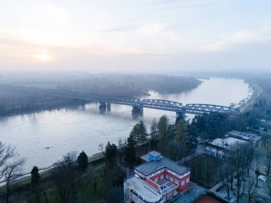 Cremona, İtalya - 9 Şubat 2025 İtalya, Cremona 'da Po Nehri' nin havadan görünüşü, sakin bir kış günbatımını Lombardy ile Emilia Romagna arasında uzanan bir köprüyle sergiliyor.
