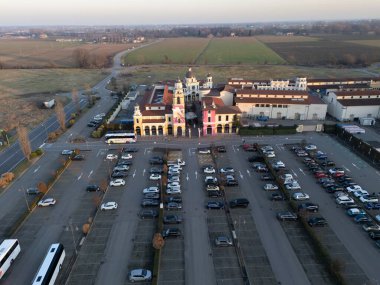 Fidenza, Italy - February 9th 2024 Aerial view capturing the Village shopping center with its expansive parking area, surrounded by fields and roads under a clear sky in February clipart