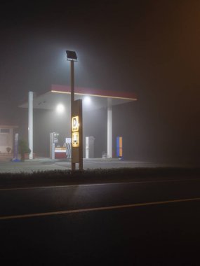 Cremona, İtalya 15 Kasım 2021 gece yoğun sis altında kalan, parlak ışıklarla aydınlatılan, gizemli ve ürkütücü bir atmosfer yaratan boş bir benzin istasyonu.