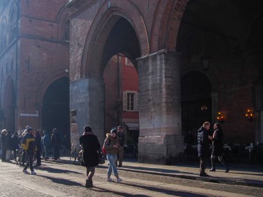 Cremona, İtalya 15 Kasım 2021 'de güneşli bir kış gününde İtalya' nın Cremona kentinde bulunan Comune Meydanı 'ndaki Palazzo Comunale' in kemerlerinin altında yürüyen turistler görülüyor.