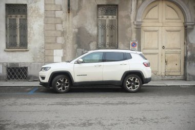 Lombardy, İtalya 1 Mart 2025 'te Cremona' da tarihi tuğla duvarın yanına park edilmiş beyaz cip pusulası, çağdaş otomotiv tasarımını klasik mimari arka planla birleştirdi.