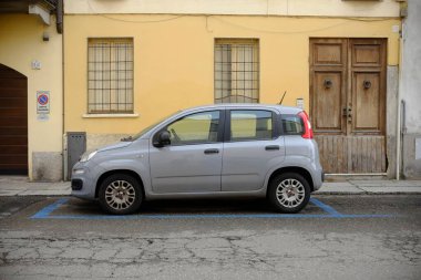 Lombardy, İtalya 1 Mart 2025 Gri Fiat Panda, İtalya 'nın Cremona kentindeki sarı bir konut binasının önündeki mavi bir otoparka doğru park etmiş.
