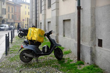 Lombardy, İtalya 1 Mart 2025 Yamaha scooter 'ı ile sarı Glovo marka termal çanta yiyecek teslimatı için Cremona, İtalya' da kaldırıma park edilmiş.