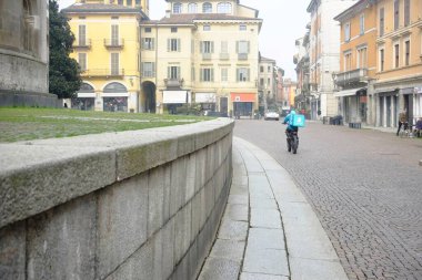 Lombardy, İtalya 1 Mart 2025 Sevkiyat sürücüsü İtalya 'nın Cremona şehrinin büyüleyici sokaklarında yiyecek teslimatı için termal bir sırt çantasıyla bir scooter kullanıyor.