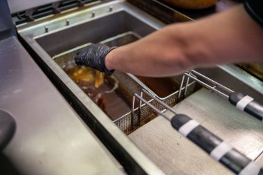 Sıcak yağa batırılmış iki sepet içeren paslanmaz çelik kızartma makinesi, hareketli bir profesyonel mutfakta geleneksel Hint yemekleri pişirmeye hazırlanıyor, aşçılık deneyimlerini geliştiriyor.