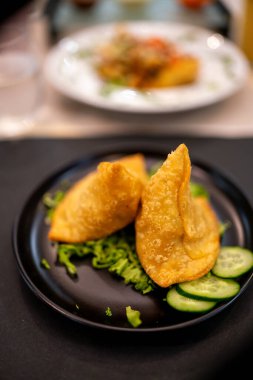 Kıtır kıtır, üzerinde canlı domates, soğan, kişniş ve kremalı sos karışımı olan altın renginde samosa, lezzetli ve görsel olarak çekici bir Hint yemeği oluşturur.