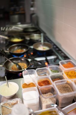 Profesyonel aşçı geleneksel Hint yemekleri pişiriyor şeffaf plastik kaplarda farklı baharatlar ve bir restoranın mutfağında tavalar kullanıyor.