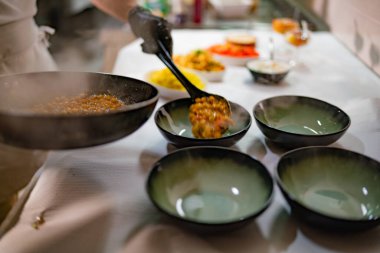 Şef bir kepçeyi ustalıkla sıcak, buharı üstünde Hint yemeği servis etmek için kullanıyor. Kalabalık bir restoranın mutfağında, bir sonraki servis için hazırlanıyor.