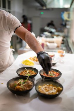 Hintli şef siyah eldiven giyip bir restoranın mutfağındaki beyaz masa örtüsünde sıcak köri tabakları hazırlıyor ve otantik Hint mutfağını servis etmeye hazırlanıyor.